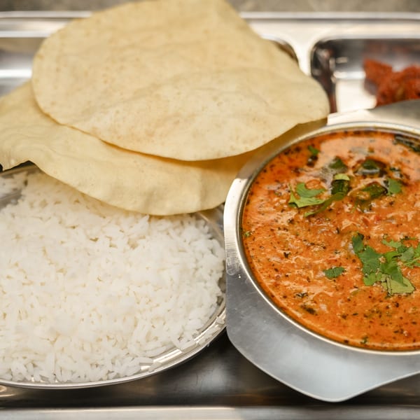 A stainless steel thali with rice, papadum, a bowl of curry, and a small dish of pickle.