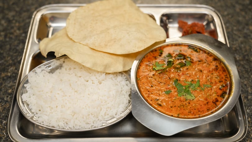 A stainless steel thali with rice, papadum, a bowl of curry, and a small dish of pickle.