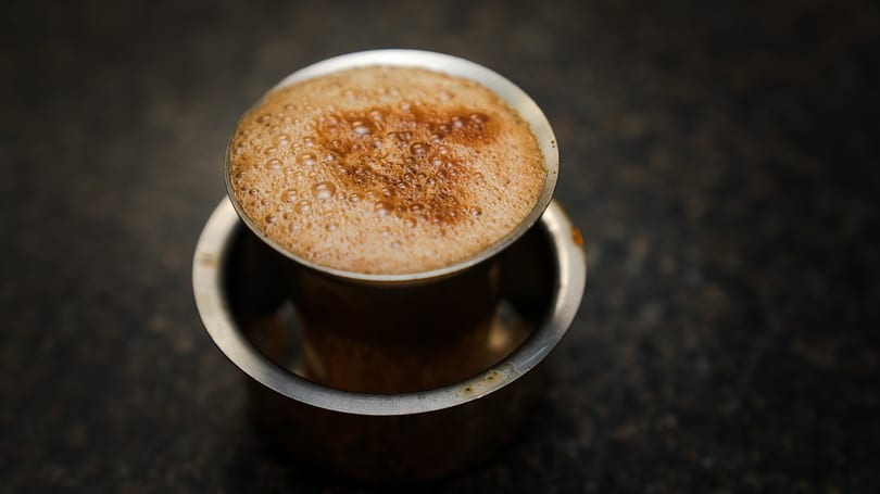 Close-up of a frothy South Indian filter coffee in a traditional metal dabara set.