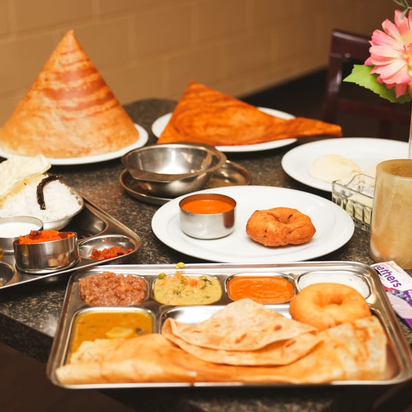 A table laden with various Indian dishes, including dosas, curries, rice, and bread.