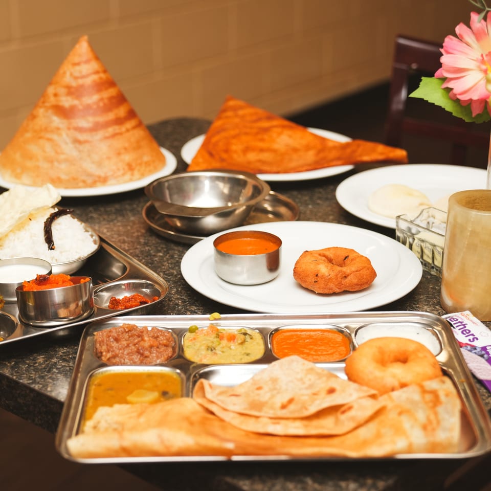 A table laden with various Indian dishes, including dosas, curries, rice, and bread.