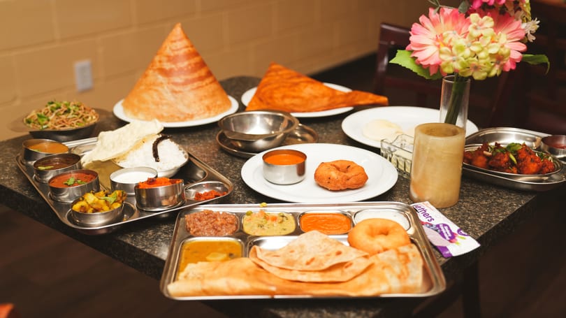 A table laden with various Indian dishes, including dosas, curries, rice, and bread.