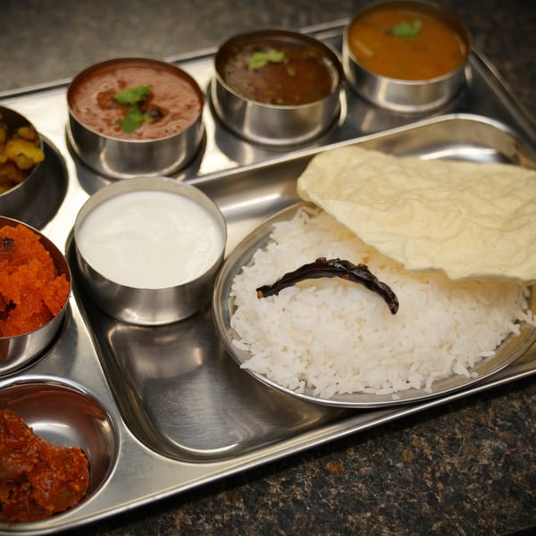 A stainless steel thali tray with various Indian dishes including rice, curries, and sweets.