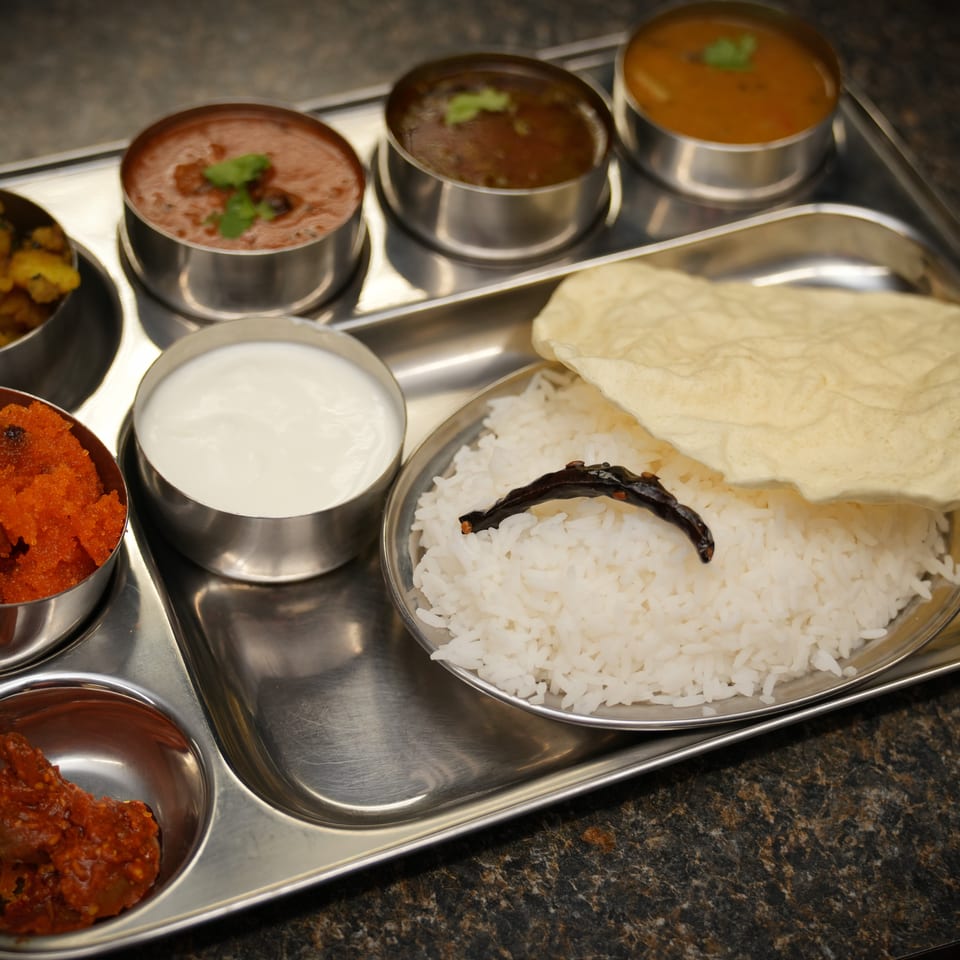 A stainless steel thali tray with various Indian dishes including rice, curries, and sweets.
